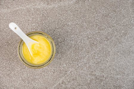 Ghee butter in a jar on a gray stone background top view, space for text.