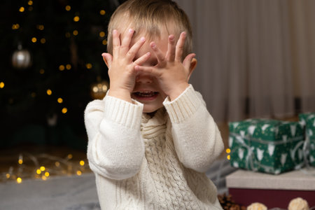 Funny toddler covering his eyes with his hands in anticipation of Christmas surpriseの写真素材