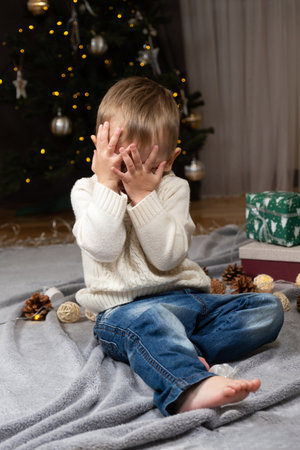 Funny toddler covering his eyes with his hands in anticipation of Christmas surprise.の写真素材