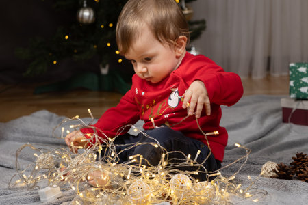 A one-year-old toddler plays with a garland at Christmas