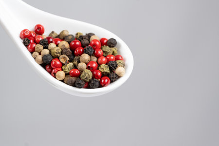 Different varieties of peppercorns, red, green, black and white peppers in a spoonの写真素材