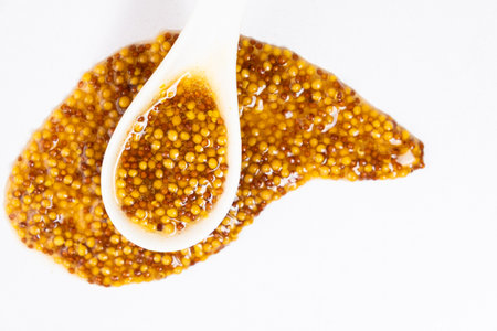 French mustard in a spoon on a white background.