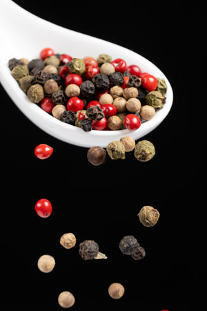 Different types of peppercorns pouring. Red, green, white and black pepper