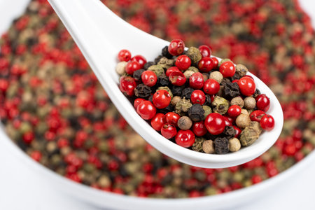 Different varieties of peppercorns, red, green, black and white peppers in a spoon.