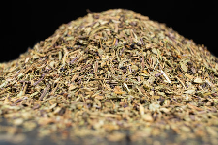 Pile of chopped dry basil seasoning on a black background