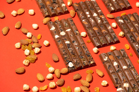 Lots of chocolate bars with nuts and raisins on a red background.の写真素材