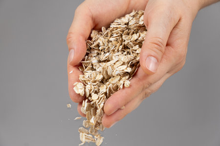Hands pouring uncooked raw oatmeal on a gray background