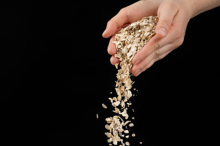 Hands pouring uncooked raw oatmeal on a black background space for text.の写真素材