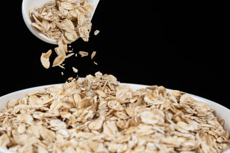 Uncooked raw oatmeal pour out of a spoon, black backgroundの写真素材