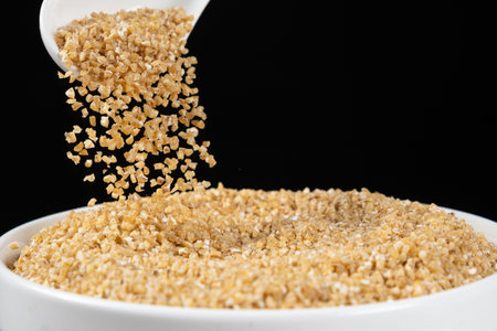 Uncooked organic wheat groats pour out of a spoon close-up.の写真素材