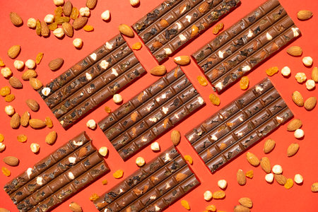 Lots of chocolate bars with nuts and raisins on a red background.の写真素材
