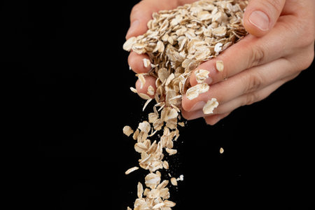 Hands pouring uncooked raw oatmeal on a black background
