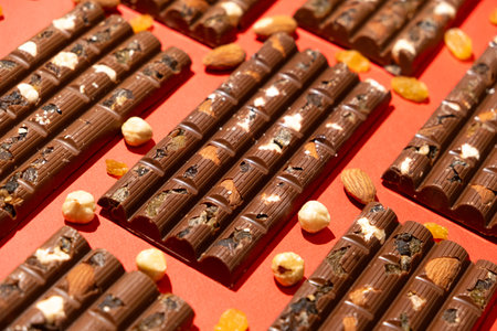 Lots of chocolate bars with nuts and raisins on a red background.の写真素材