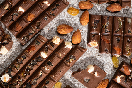 Broken chocolate pieces with nuts and raisins on a stone background top view.