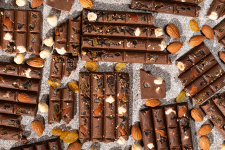 Broken chocolate pieces with nuts and raisins on a stone background top view.の写真素材