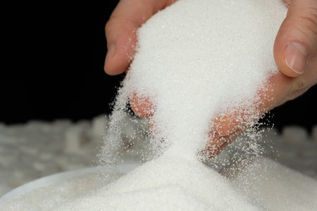 Hands pouring white crystalline refined sugar, black background.の写真素材