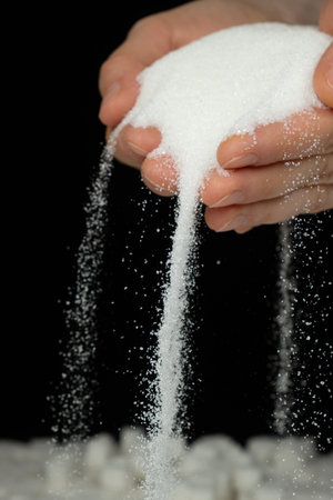 Hands pouring white crystalline refined sugar, black background.の写真素材