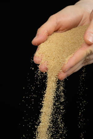 Hands pour crystalline cane brown unrefined demerara sugar.