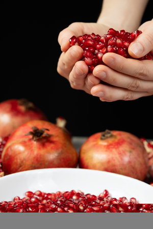 Handful of pomegranate seeds, pomegranate seeds in hands, black background.の写真素材