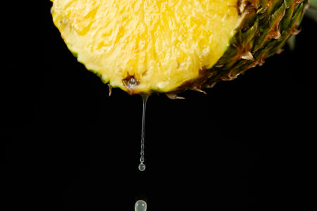 Pineapple juice running down the cut of fresh pineapple fruit on a black background.の写真素材