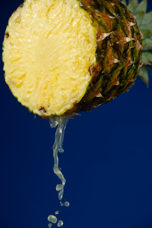 Pineapple juice running down the cut of fresh pineapple fruit on a blue background.の写真素材