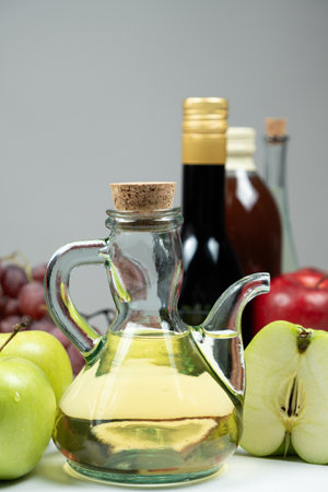 Apple cider vinegar in a vinegar cruet with spout on the background of other types of vinegars and fruitsの写真素材