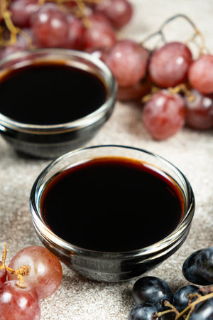 Balsamic vinegar poured into a glass sauce dish among the grapes.の写真素材