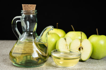 Apple cider vinegar in a glass vinegar bowl among apples.
