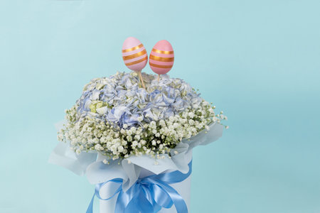Two Easter painted eggs in a bouquet of flowers on a blue background, copy space for text.
