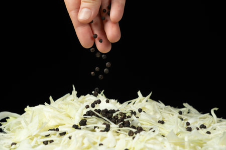 Sprinkling black peppercorns on chopped white cabbage.