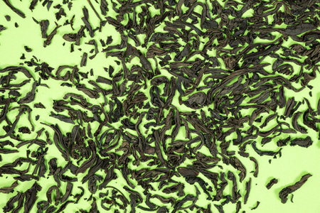 Scattered leaves of black large leaf tea on green background top viewの写真素材