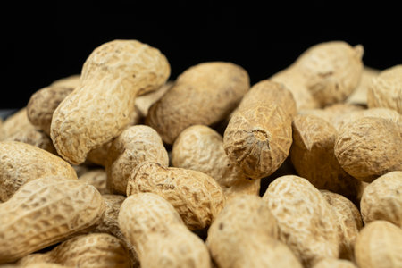 Pile of unpeeled peanuts in shell close-up on black background.