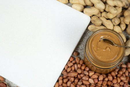 Peanut butter in a jar among scattered peanuts, space for text