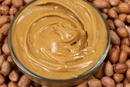 Peanut butter in a bowl among scattered peanuts.