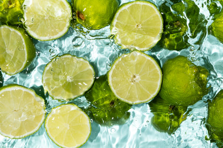 Bright fruity summer background of halves of fresh limes in water top view.の写真素材