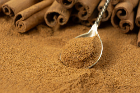 Close-Up of Spoonful of Brown Ground Spice and Cinnamon Sticks. Natural Food Scene