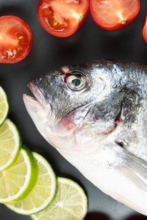 Fresh Whole Dorado Sea Bream Fish with Cut Limes and Tomatoes.