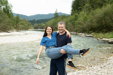Happy young married couple, husband holding wife in arms in nature near river.の写真素材