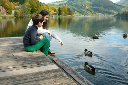 Mother with Son Watching Ducks on the Lake. Spending Time Together in Natureの写真素材