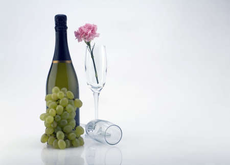 A bottle of champagne with grapes and a carnation in a glass flute. の写真素材