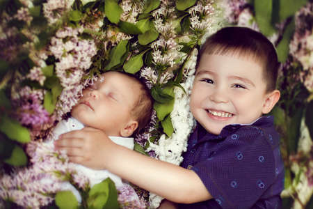 happy older brother of three years, embracing his baby sister on the background color of lilacの写真素材