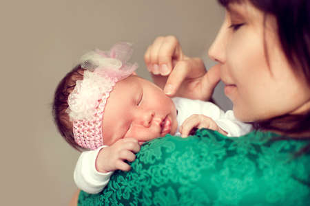 Young Asian mother holding the shoulder of the baby, which is sleeping and gently strokes her cheek with a fingerの写真素材