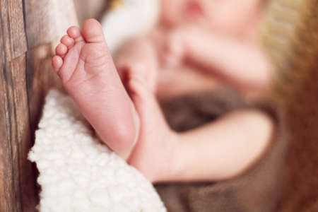 Little white feet of a newborn baby who sleeps in a basket on a white blanket