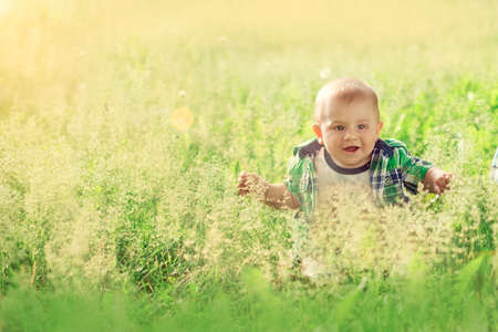 little baby boy sitting summer outdoors grass in sun and enjoy the warmth and laughs