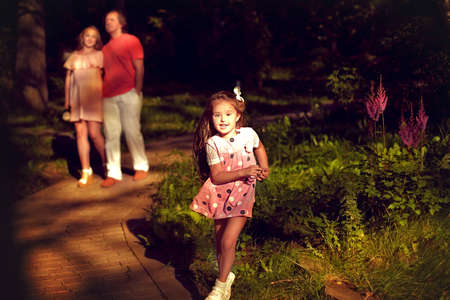 cheerful girl with long hair running around and playing in summer Park with their parents. The stay...