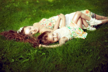 beautiful girl with long hair lying next to his pregnant mother in the summer on the green grass. Stay for the weekendの写真素材