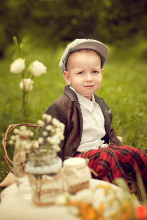 little boy in a jacket and plaid pants to sit on the cushion, next to a bouquet of wild flowers, the old days, a child in a retro styleの写真素材
