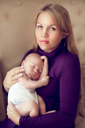 Young beautiful mother holding sleeping newborn baby on hands in the bedroom. The woman lulls son pressed against his chest. Happy family at home.の写真素材