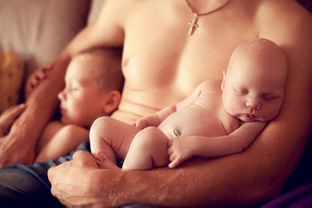Newborn baby asleep in the arms of a strong father along with his elder brother. The children sleep...
