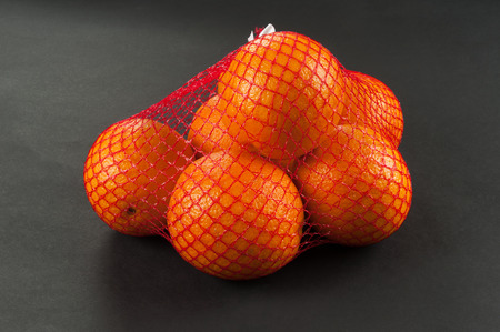 oranges in bag mesh on dark backgroundの写真素材